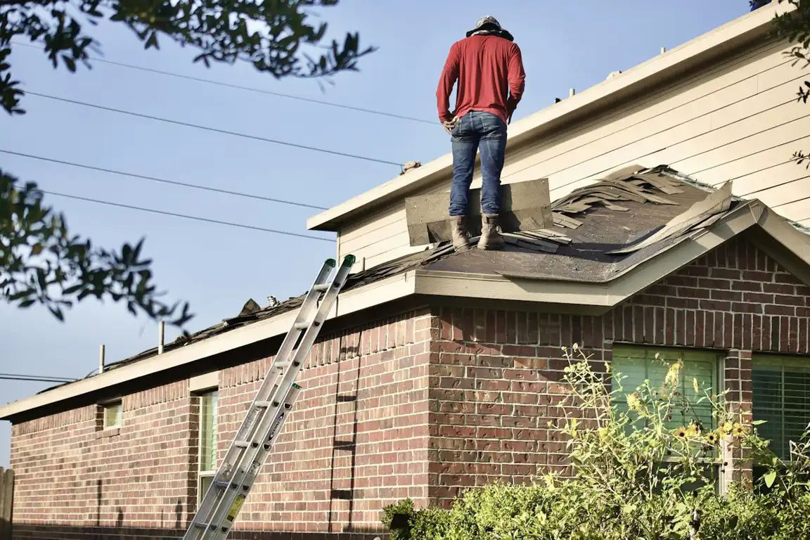 Roofer removing worn shingles from a Palm Beach County home during a roof replacement